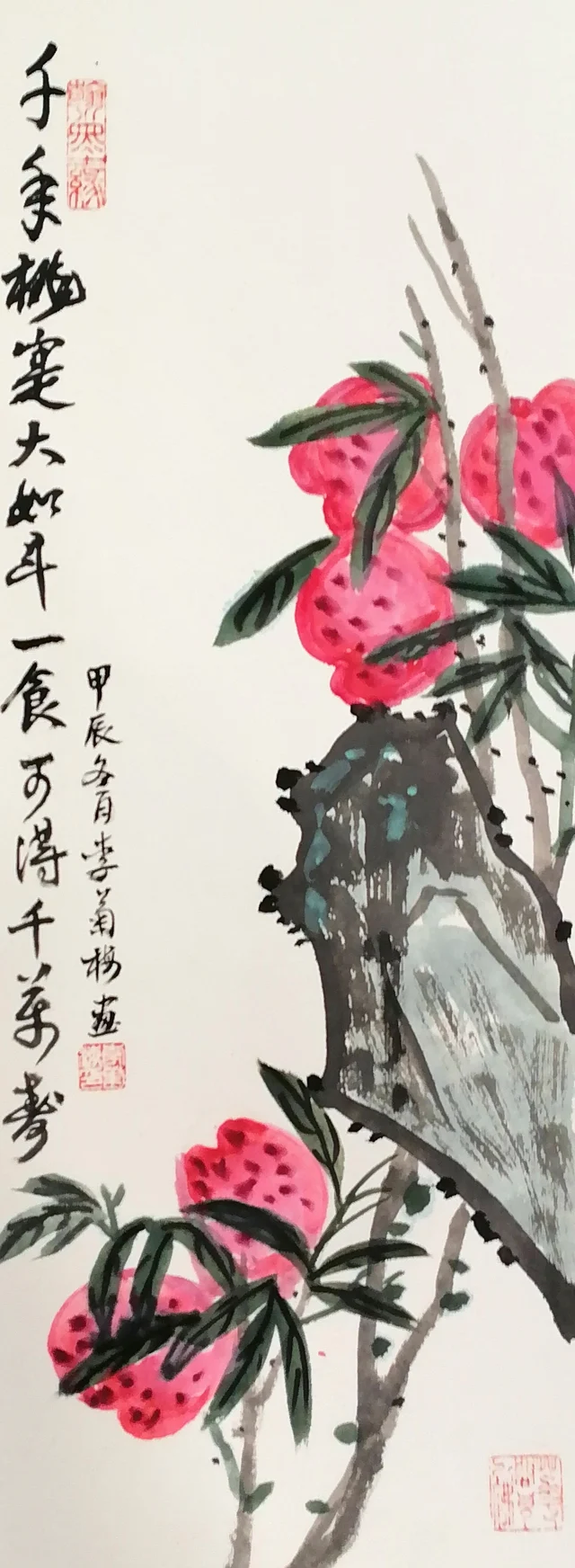 A tall narrow painting on card of red peaches on a branch behind a grey-blue garden rock at the right, with two columns of calligraphy on the left.