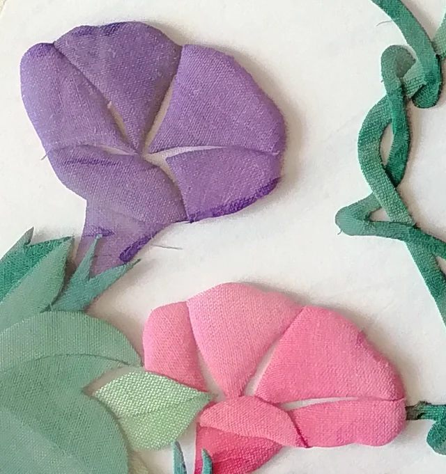 A purple and a pink flower among overlapping leaves.