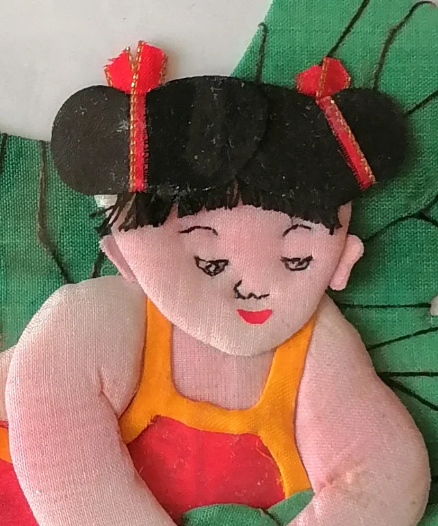 The child’s face, drawn in ink, with red ribbons on the topknots.