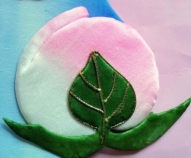 The peach, pink shading to white, under a leaf veined in gold thread.
